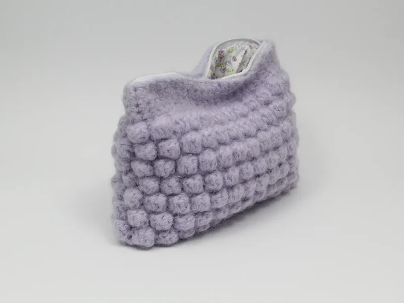 Beauty case crochet lilla, foderato in tessuto di cotone con motivo floreale.