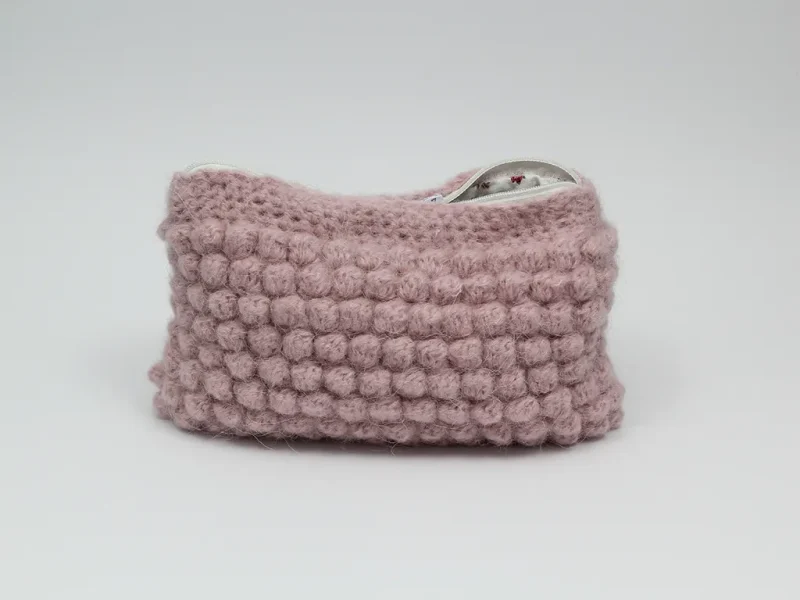 Beauty case crochet rosa baby, in lana baby alpaca, con cerniera bianca e foderato in tessuto di cotone a motivo floreale.