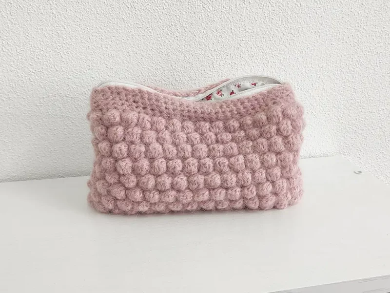 Beauty case crochet rosa baby, in lana baby alpaca, con cerniera bianca e foderato in tessuto di cotone a motivo floreale.