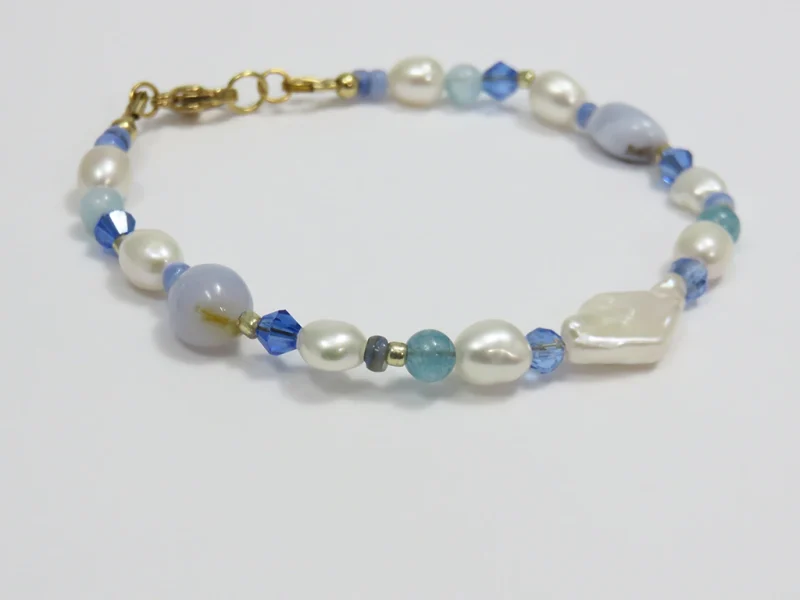 Bracciale con perle blu, pietre di agata blu lace levigate e perle di fiume irregolari, con perla bianca a forma di rombo, con chiusura a moschettone dorata.