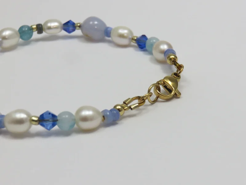 Bracciale con perle blu, pietre di agata blu lace levigate e perle di fiume irregolari, con perla bianca a forma di rombo, con chiusura a moschettone dorata.