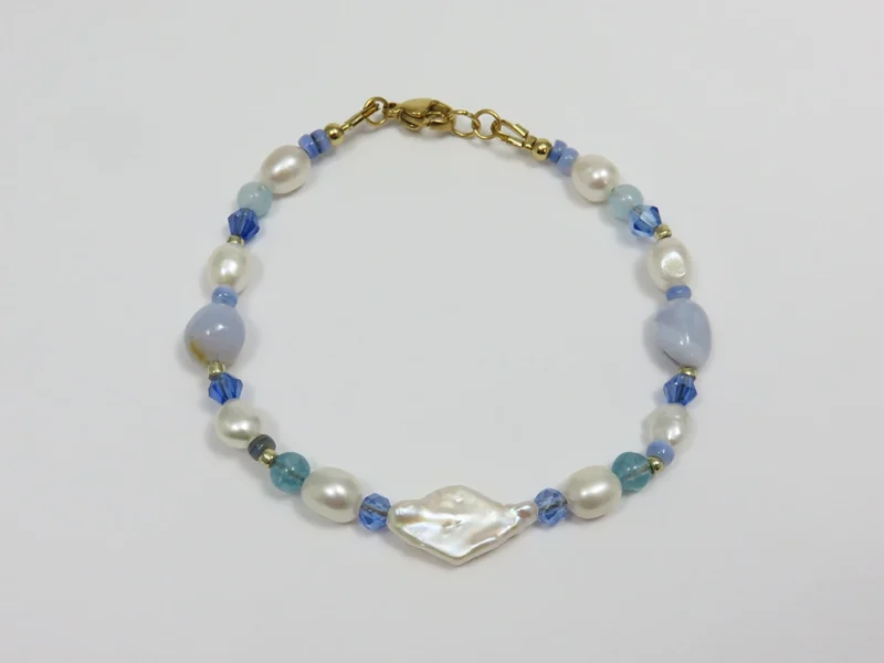 Bracciale con perle blu, pietre di agata blu lace levigate e perle di fiume irregolari, con perla bianca a forma di rombo, con chiusura a moschettone dorata.