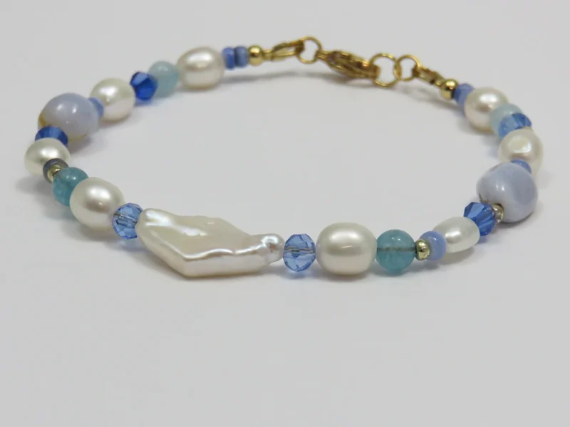 Bracciale con perle blu, pietre di agata blu lace levigate e perle di fiume irregolari, con perla bianca a forma di rombo, con chiusura a moschettone dorata.