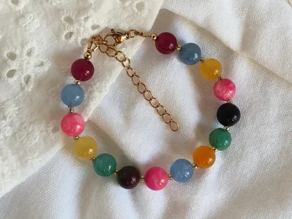 Bracciale con perle colorate, con chiusura a moschettone e catenella di estensione dorata.