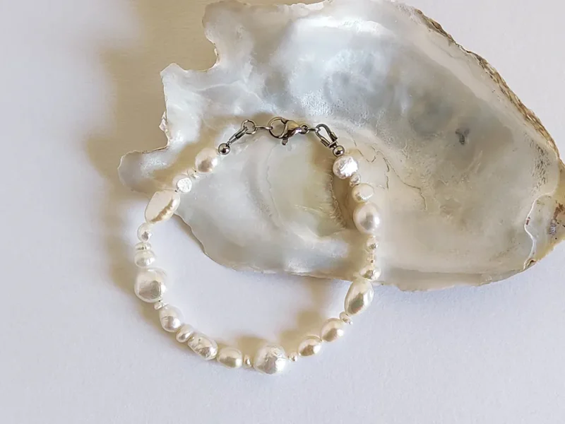 Bracciale di perle di fiume irregolari, con chiusura a moschettone, posato su piano bianco.