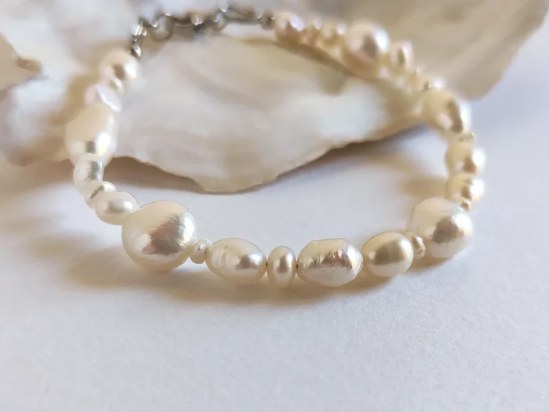 Bracciale di perle di fiume irregolari, con chiusura a moschettone, posato su piano bianco.