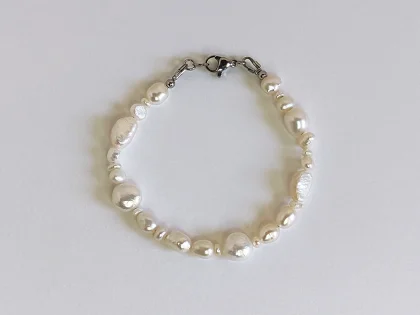 Bracciale di perle di fiume irregolari, con chiusura a moschettone, posato su piano bianco.