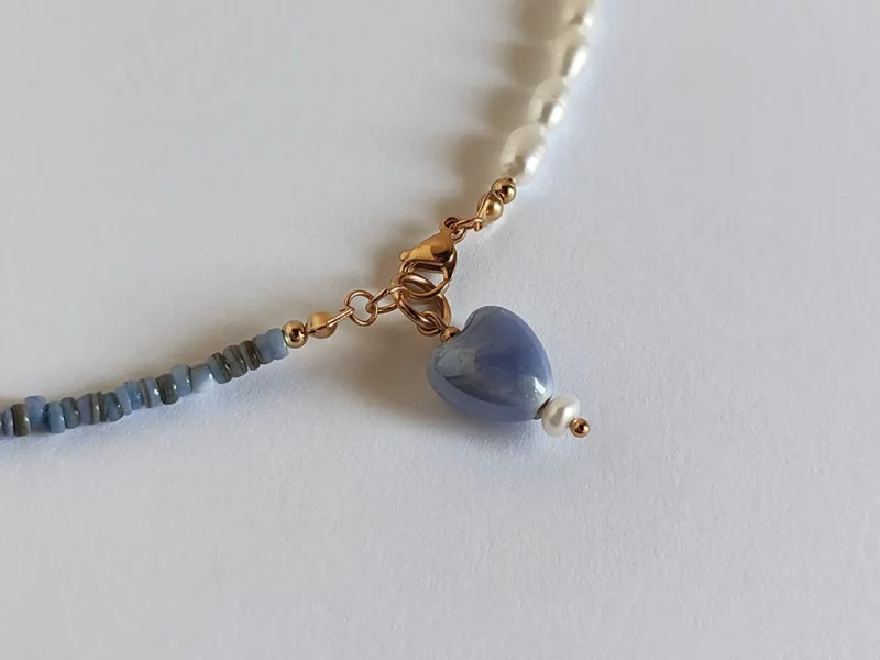 Collana metà perle e metà madreperla blu, con chiusura a moschettone dorata in acciaio inox e ciondolo a forma di cuore finale.