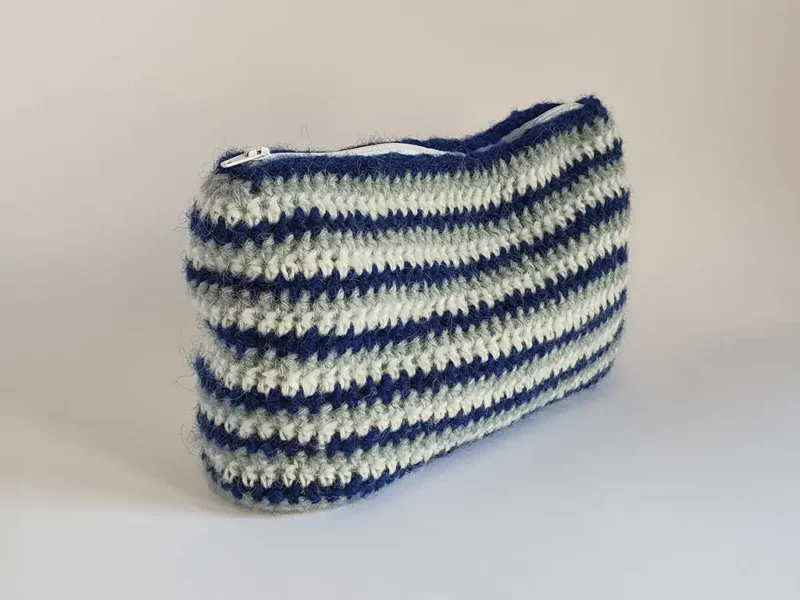 Beauty case crochet a righe blu, in lana di baby alpaca, foderata in cotone e con cerniera a zip.