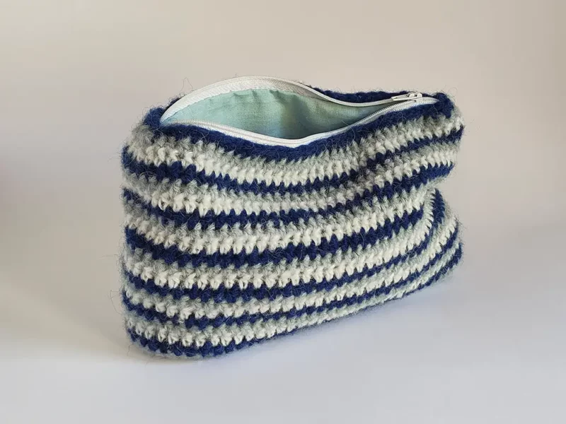 Beauty case crochet a righe blu, in lana di baby alpaca, foderata in cotone e con cerniera a zip.